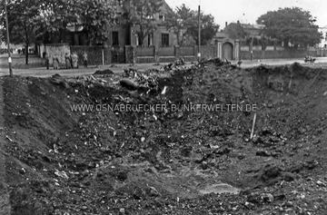 Einschlagstelle des am 18. September 1940 abgeschossenen britischen Vickers-Wellington-Bombers am Stahlwerksplatz. Im Hintergrund die Eisengießerei und Maschinenfabrik von H. W. Ortmann, Buersche Straße 95-103e. links die Einmündung in den Kanonenweg. Im Osnabrücker Tageblatt vom 20.9.1940 wurde diese Aufnahme mit folgendem Vermerk abgedruckt: "Am Rande eines Kraters von etwa 10 Meter Durchmesser und etwa 4 Meter Tiefe liegen die Trümmer des abgeschossenen englischen Flugzeugs" Vickers-Wellington Stahlwerksplatz