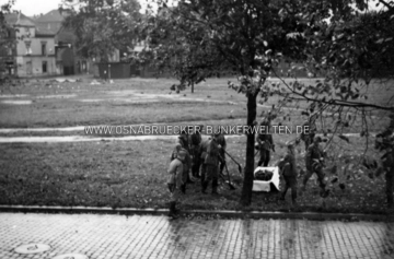 Soldaten beim Einsammeln sterblicher Überreste der britischen Bomber-Besatzung, die am 18.9.1940 am Stahlwerksplatz mit ihrer Maschine in den Tod stürzte. Auf der Rückseite des Fotos wurde nüchtern vermerkt: "Das einsacken der Toten". Im Hintergrund ist die Buersche Straße und die Einmündung in den Kanonenweg zu erkennen. Soldaten suchen sterbliche Überreste am Stahlwerksplatz