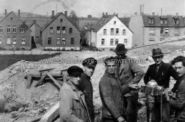 Bauarbeiter bei Ausschachtungsarbeiten für den Stollenbunker an der Quellenburg. Im Hintergrund sind (von rechts nach links) die Häuser Sutthauser Straße 218 - 224. Bauarbeiter an der Quellenburg