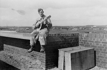 Ein Soldat auf einer Umfassungsmauer einer Flak-Stellung auf dem Kalkhügel. Im Hintergrund rechts ist die Anhöhe des Schölerbergs zu erkennen. Soldat auf Umfassungsmauer Flak-Stellung