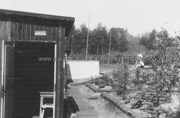 Blick auf eine Baracke in der Flak-Stellung bei Achmer, Mai 1942. Im Hintergrund ist ein getarnter Flak-Hochstand zu erkennen. Baracke und Flakturm Achmer